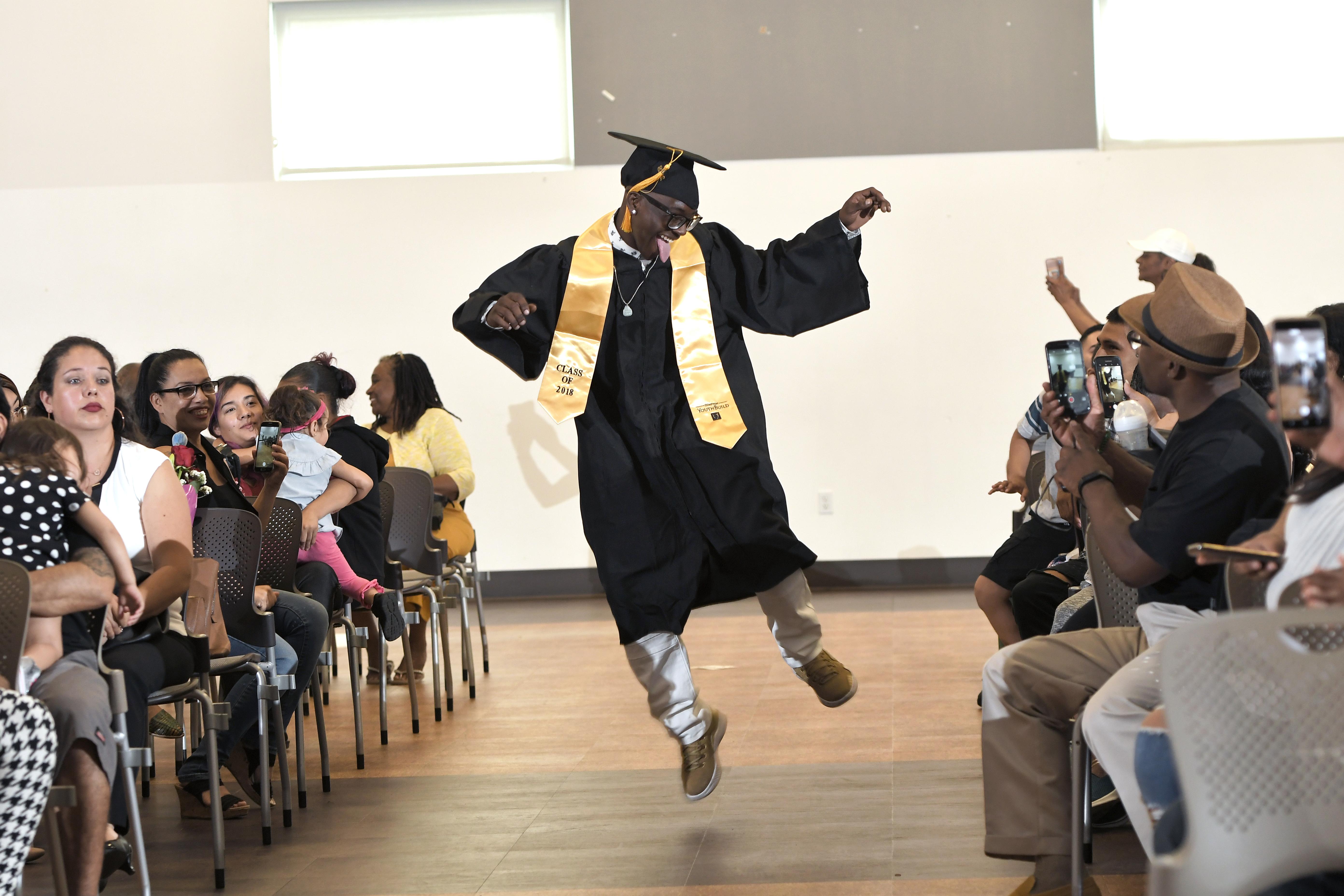 a Compton graduate in his cap and gown jumps for joy