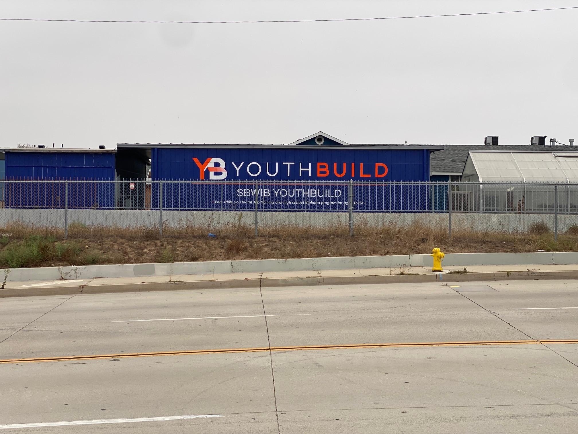 Photo of the new sign painted on the blue building at SBWIB YouthBuild. The sign reads "SBWIB YouthBuild - Earn while you learn. Job training and high school diploma program for ages 16-24"