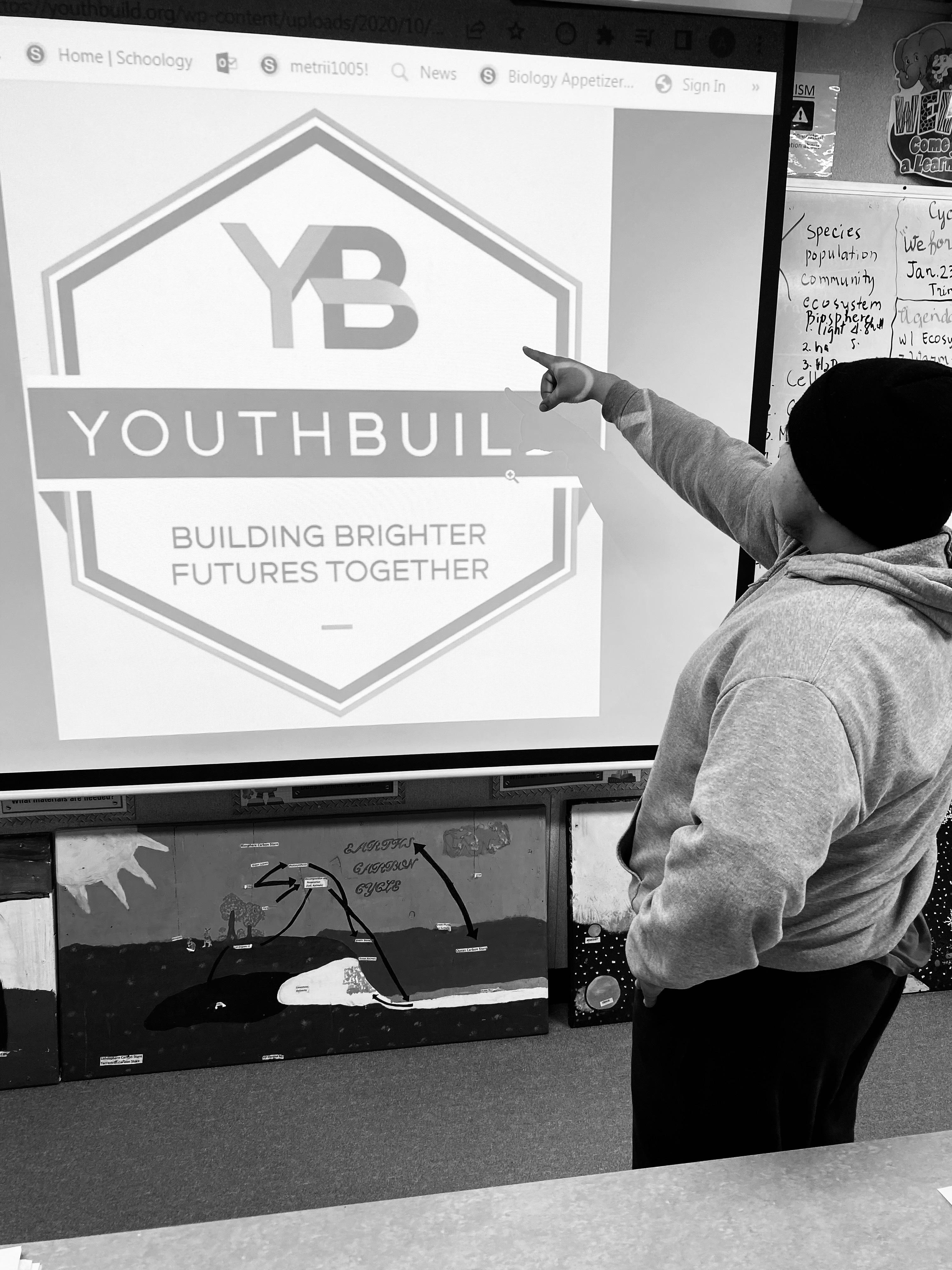 A black and white photo of a s student standing in front of a projection with the YouthBuild logo