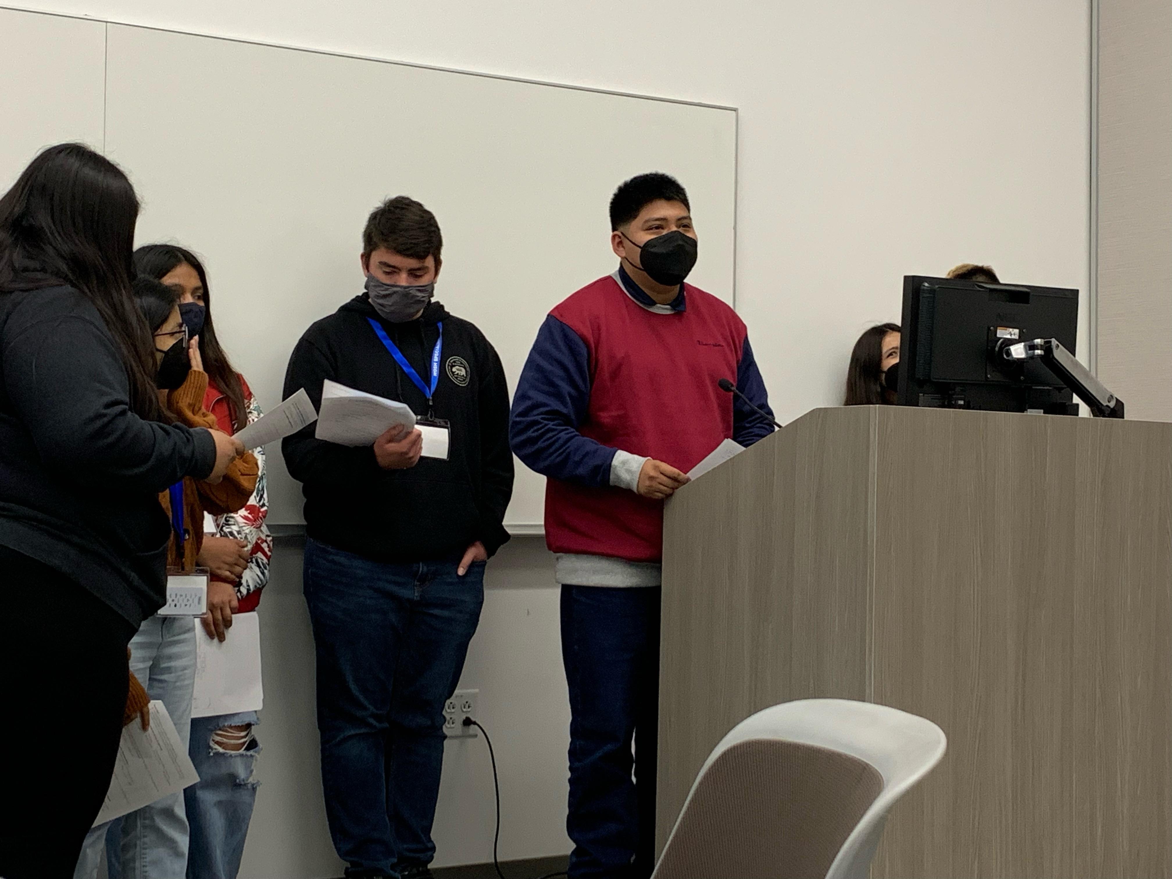 a student wearing a mask stands at a podium