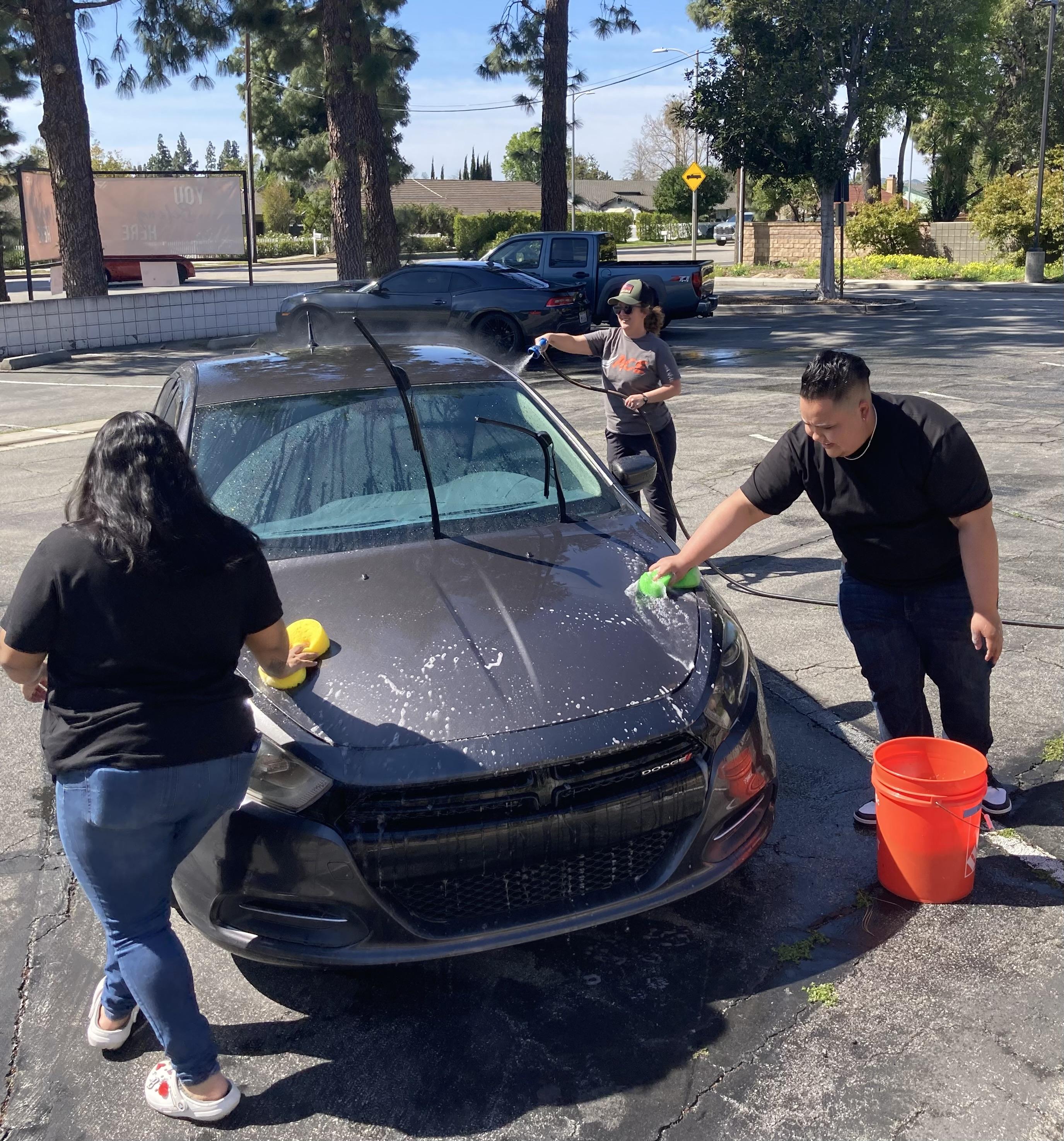 2 students and Ms. Ashley washing a car